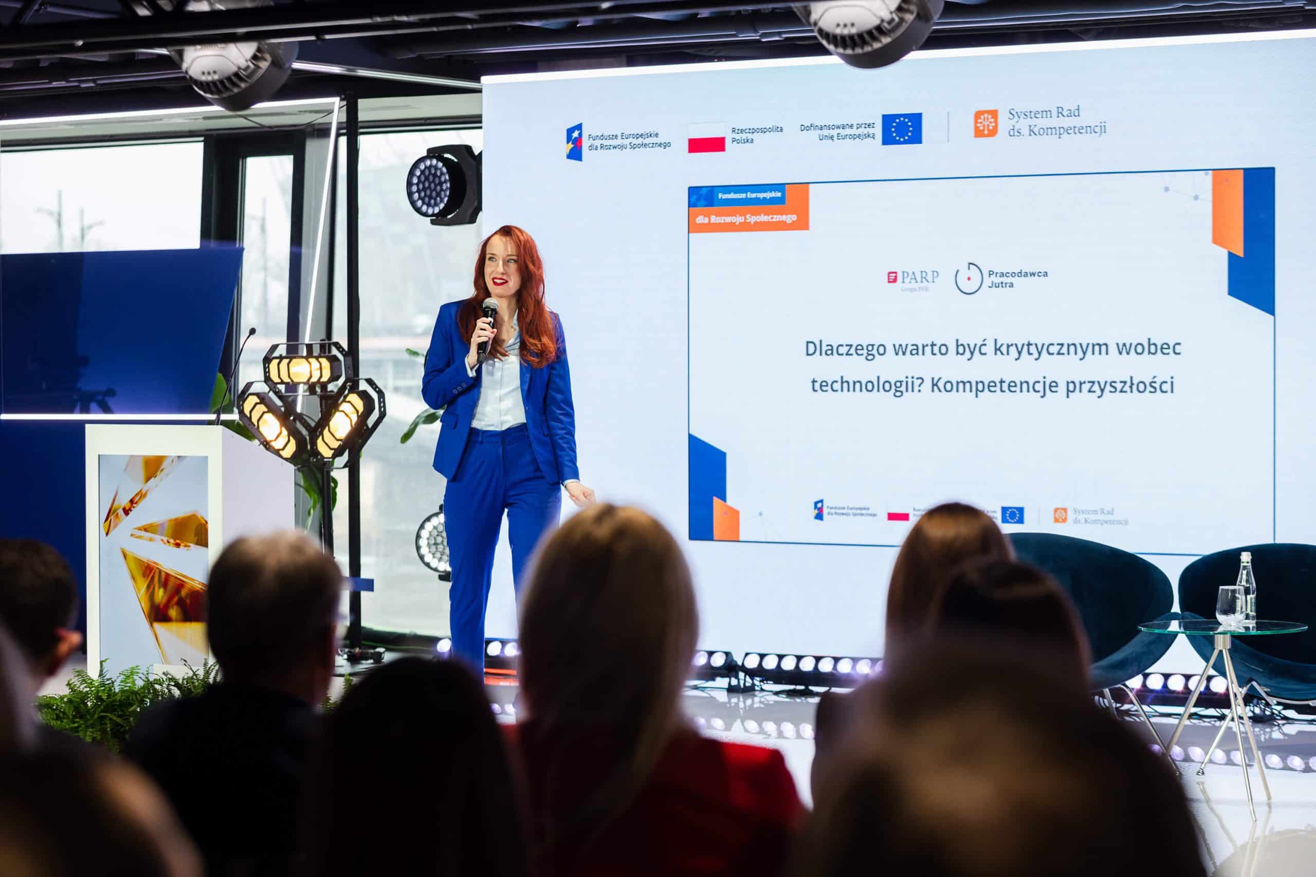 Anna Prończuk-Omiotek z mikrofonem na scenie konferencji przed pełną salą